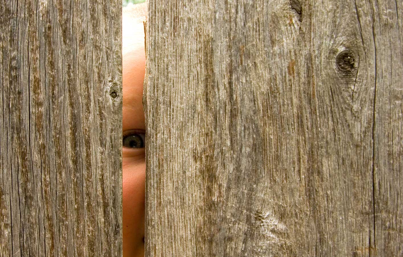 Kind schaut durch Holzzaun